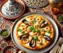 Italiaanse pizza met zeevruchten geserveerd op een Marokkaanse tafel, met Tajine.nl decoratief verwerkt in de tajinedeksel.